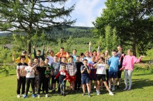 Спільне фото дітей з громад Донеччини. На фоні смерек та Карпатських гір діти посміхаються та машуть руками.
