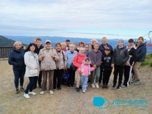 Чоловіки та жінки з дітьми на вершині гори. Позаду них гори та блакитне небо.
