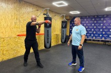 Доцент кафедри спеціальної фізичної підготовки Володимир Галімський, допомагає у реабілітації. Чоловік у чорній футболці тримає гірі у руках та робить вправи
