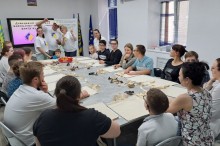 Учасники майстер-класу сидять за великим столом, уважно слухаючи інструкції та готуючись до творчої роботи зі штампами