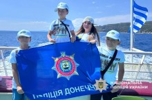 Діти на катері. У білих футболках та кепках тримають прапор поліції Донеччини.