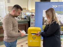 Представники Покровської громади стоять біля поштової скриньки жовтого кольору та відправляють листи.