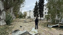 Правоохоронець стоїть у дворі біля зруйнованого будинку