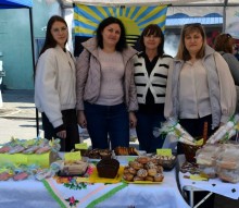 Жінки біля столу. Позаду прапор Донеччини. На столі продукція.