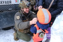 Поліцейський підрозділу «Білий янгол» одягає помаранчеву каску на дитину.