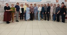 Учасниці заходу позують для фото в ряд біля виставочних банерів, одна з них тримає піднос із випічкою