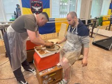 Чоловік сидить біля гончарного кола, поки майстер показує йому процес роботи з глиною