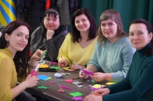 П’ять жінок сидять за столом і вирізають фігурки з кольорового паперу та фетру.