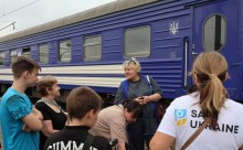 Волонтери та евакуйовані родини з дітьми стоять біля евакуаційного потяга.