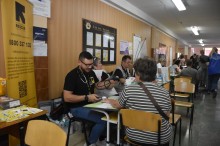 Жінка сидить за столом, напроти лікар, який міряє тиск. Дія в транзитному хабі.