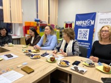 Чаювання. Жінки сидять за столом, спілкуються, на столі чай та солодощі. Позаду банери організаторів зустрічі.