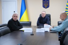 Робоча група сидить за столом та заслуховує доповідь.
