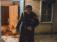 Евакуйована остання мешканка села Новокриворіжжя Криворізької громади — жінка 1956 року народження. Жінка тримає на руках цуценя. Стоїть біля будинку.