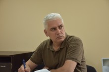 Учасник робочої зустрічі. Сидить за столом та тримає ручку.