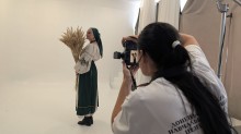 Фотографиня знімає жінку в українському етнічному вбранні та зеленій хустці, яка тримає оберемок сухоцвітів