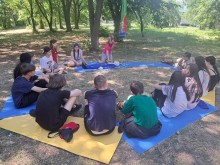 Група підлітків на килимках у формі слухає інструктаж з домедичної допомоги в лісі під час вишколу «Січ незламних».