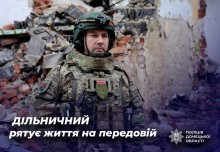 Дільничний офіцер громади у камуфляжі, на задньому плані - будівля, яка постраждала від обстрілів