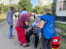 Працівник швидкої допомоги та працівник благодійної організації надають першу медичну допомогу літній жінці.