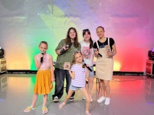 Діти та дорослі співають на сцені з мікрофонами