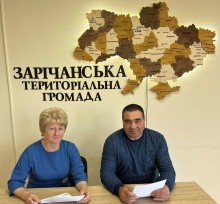 Посадовці Комарської та Зарічанської громад сидять за столом на фоні дерев'яної мапи України