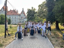 іти сидять на валізах у білих футболках, позаду них замок та зелені дерева.