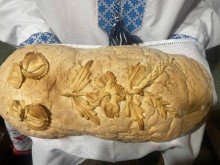 Домашня хлібина в руках юнака, прикрашена колоссям пшениці й квітами з тіста