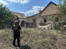 Правоохоронець стоїть біля пошкодженого паркану та будинку після обстрілу.