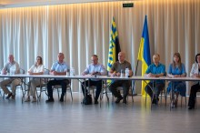 Учасники зустрічі сидять в ряд за столами.