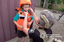 Поліцейський допомагає дитині вдягнути бронежилет та каску