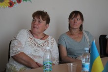 Під час відкритої зустрічі у Дружківській міській територіальній громаді: сидять 2 жінки за столом, які приймають участь у відкритій зустрічі з ветеранами та членами родин загиблих (померлих) Захисників і Захисниць. Вони уважно слухають доповідача, який доповідає онлайн.