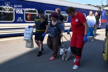 Рятувальниця та медик супроводжують жінку з собакою, яку зустріли з евакуаційного потяга
