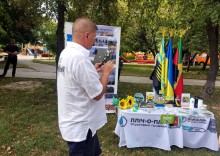Дія на вулиці. На столі сувеніри поруч прапори громад та Донеччини. Поруч стоїть чоловік.