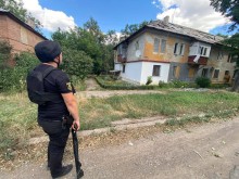 Правоохоронець біля двоповерхового будинку з пошкодженими балконами та покрівлею.