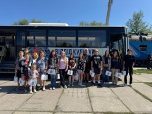 Спільне фото дітей. Діти стоять біля автобуса  та тримають в руках паперові пакети з логотипом громади.