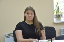 Учасниця наради. Сидить за столом в руках ручка та поруч щоденник.