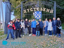 Спільне фото. Переселенці біля воріт краєзнавчого музею. На задньому плані герб міста та надпис Хустський.