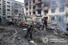 Вибухотехніки у повній екіпіровці біля пошкоджених будинків збирають уламки.