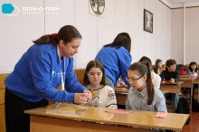 Дівчата сидять за партою, вчитель допомогає зробити Великодні свічки.