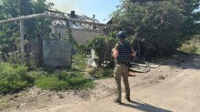 Правоохоронець стоїть на фоні зруйнованого паркану та будівлі.