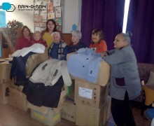 Людям похилого віку та з інвалідністю надана гуманітарна допомога у вигляді осінньо-зимового одягу. Чоловіки та жінки стоять біля ящиків з одягом.