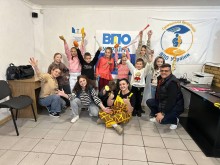 Діти та дорослі у центрі кімнати, де позаду на прапорі написано: ВПО