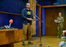 Учасник премії стоїть на сцені, в руках диплом.