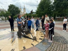 Діти біля сонячного годинника. Екскурсовод рукою показує напрямок сонячного світла. Діти уважно слухають.