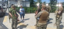 Військовослужбовці та гід на фоні стіни заповідника, пошкодженої осколками
