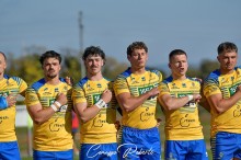 Збірна команда України з регбілігу, одягнені у жовто -блакитну форму, співають гімн України, руки тримають біля серця.