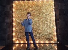 Юний учасник конкурсу співає на фоні золотої рамки