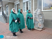 Троє жінок у зелених накидках стоять біля розписного каменю.