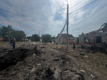 Вирва від обстрілу, поруч з якою стоять люди та зруйновані будинки