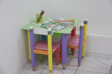Дитячий куточок.
Різнокольоровий стіл та стільці. 
На столі лежать розмальовки та олівці.