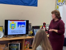 Дві жінки біля екрану монітора. Одна з них розповідає про картину на екрані. На столі кукла мотанка в українському стилі.